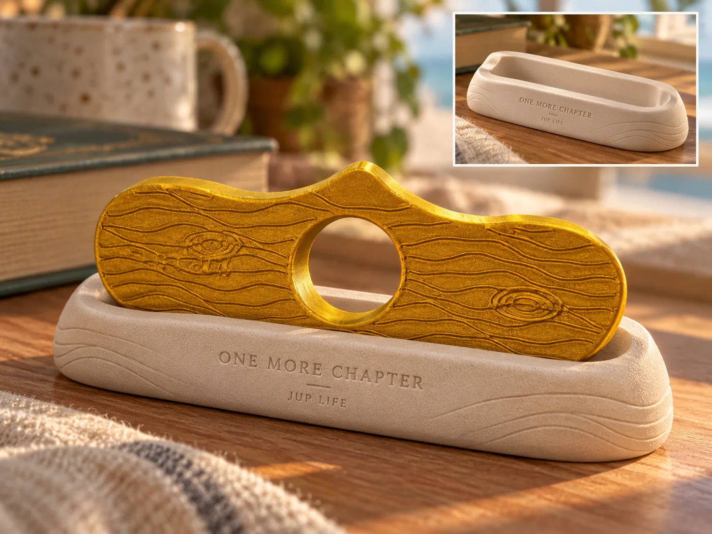 The Readers gold driftwood-pattern page holder resting in its sand-colored One More Chapter cradle, with the empty cradle inset