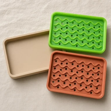 Swappable Tide soap dish inserts in lime and terracotta beside a sand base